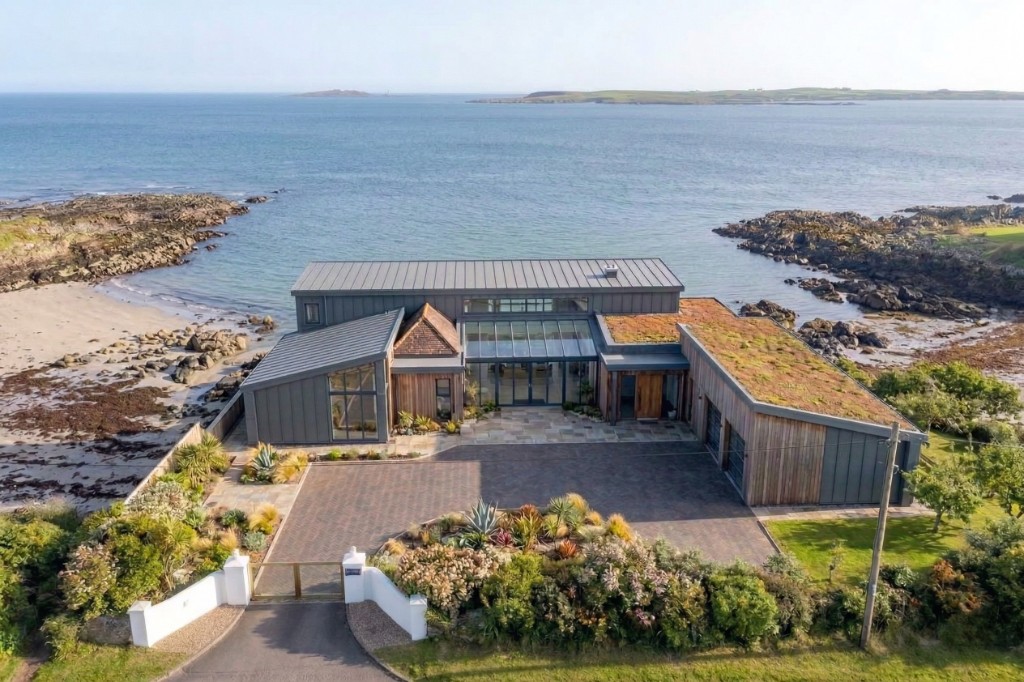 Aerial view of a modern beachfront home with ocean and landscaped grounds