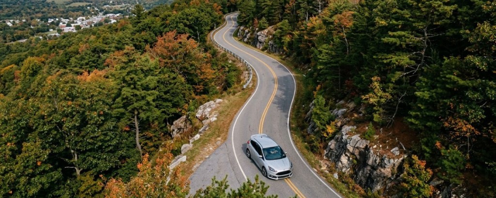 Aerial view of a silver car on a winding mountain road through forest